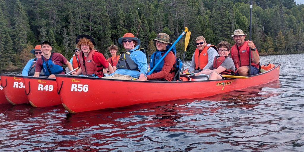 Troop 229 Scouts and leaders smiling in red canoes on a lake